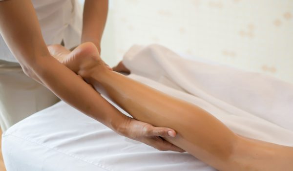 Close Up of massage therapist massaging female leg at spa salon.