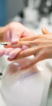 Manicure master in pink gloves applying nail varnish to female client, beauty salon. Manicurist doing fingernail care cosmetic procedure