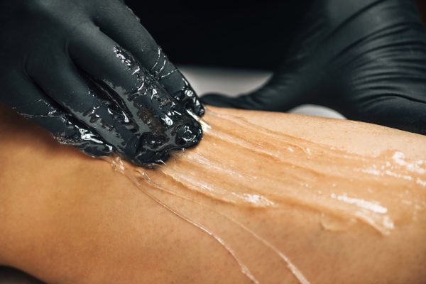 Sugaring Legs or Sugar Paste Depilation for Legs. Hand of Cosmetologist in Black Gloves Applying Sugar Paste on Female Client Close-Up