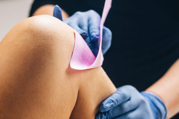 Waxing - Beautician Removing Unwanted Hair from Female Leg with Wax Strips in a Beauty Salon